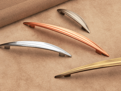 Metallic curved drawer handles in silver, copper, bronze, and gold tones displayed on a soft beige fabric surface.